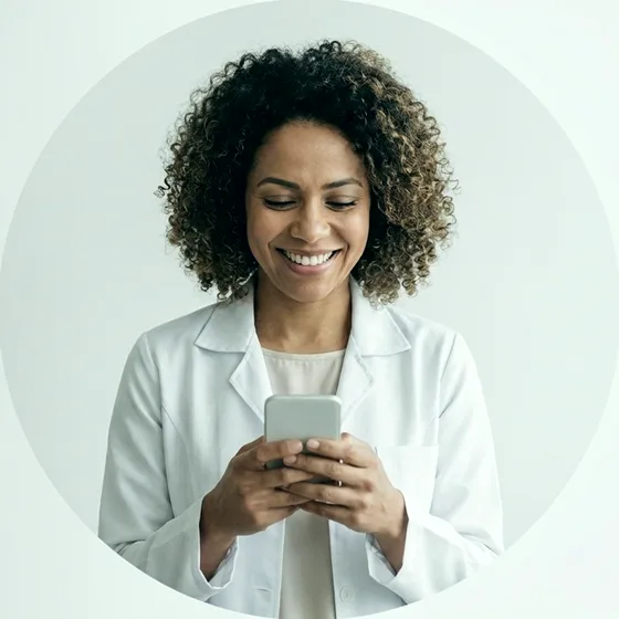 Médica sorrindo com o celular na mão (imagem ilustrativa)